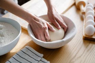 Mains d'un boulanger repliant un paton sur un plan de travail farine